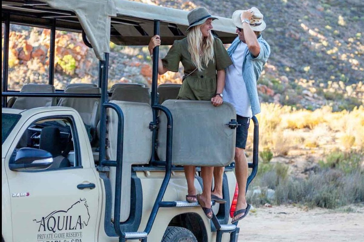 Aquila Safaris FAQs - Frequently Asked Questions and Answers Page featuring a couple standing on the side of a safari vehicle