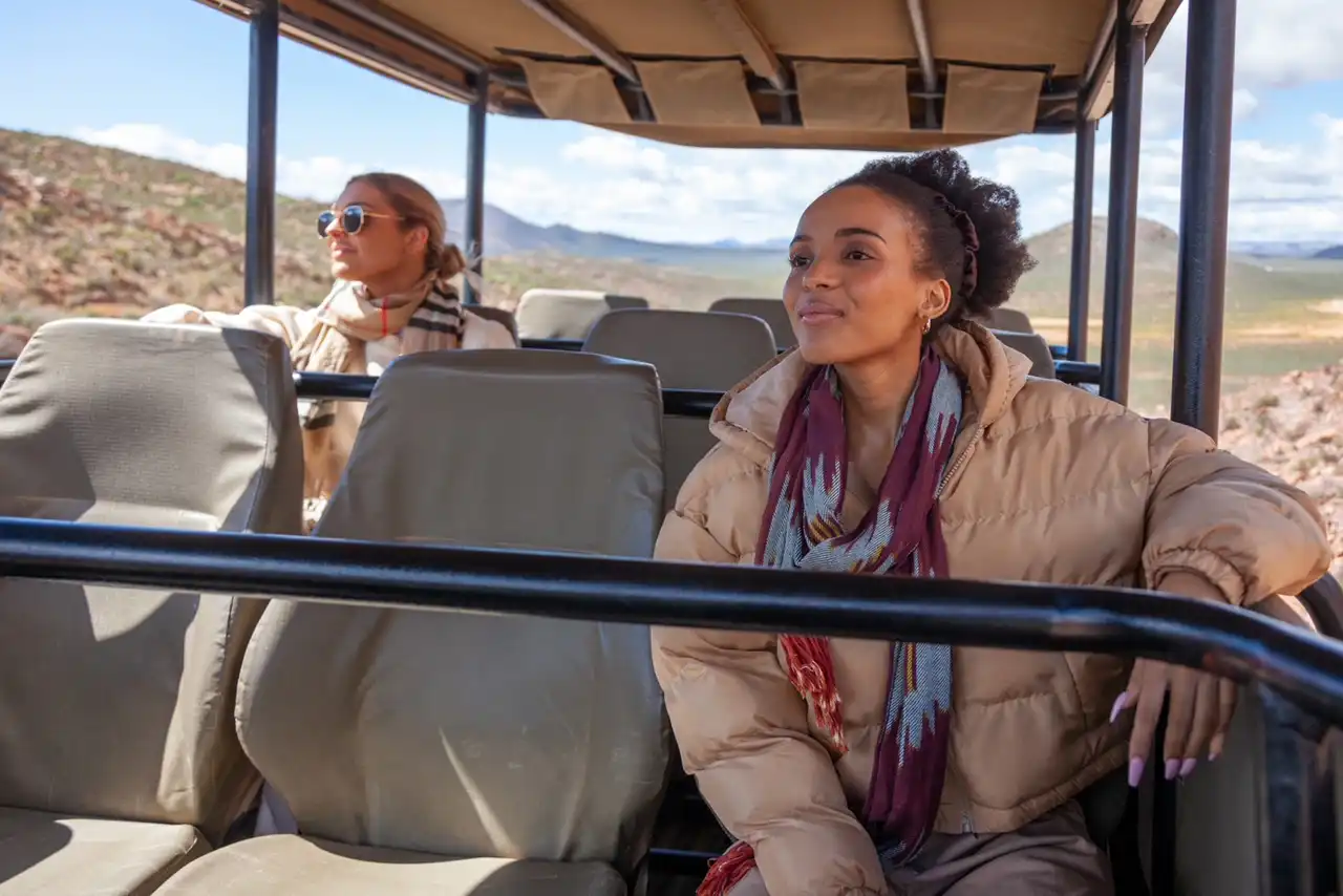 two women dressed for cold or winter weather while sitting on a traditional Big 5 safari vehicle at Aquila.